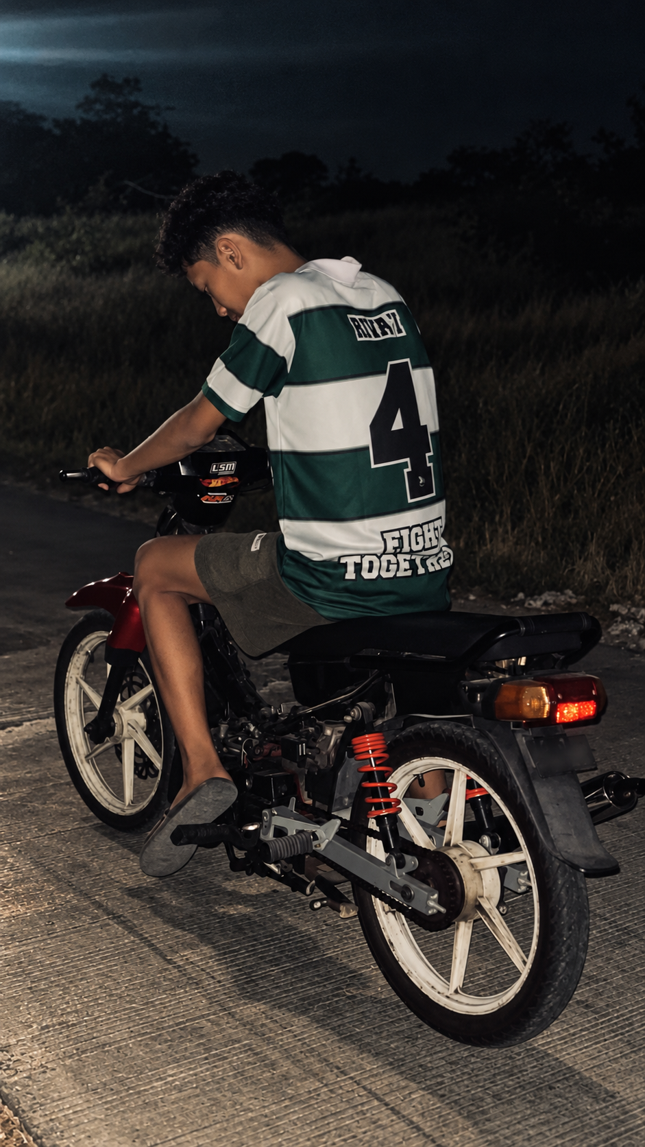 Rivai dengan jersey hijau putih duduk di atas motor pada malam hari